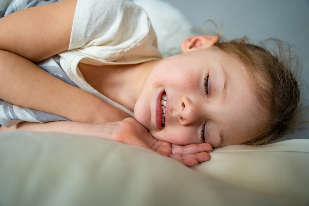 A child showing signs of bruxism by clenching and grinding her teeth while sleeping. 