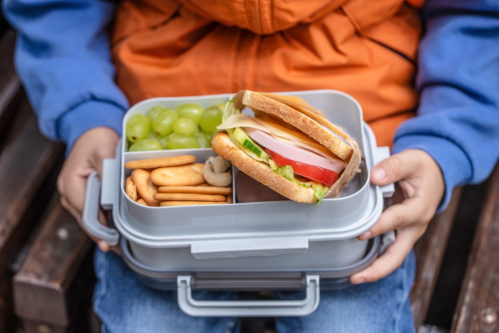 A child sitting with their lunchbox open, showing a range of healthy food for teeth and energy.