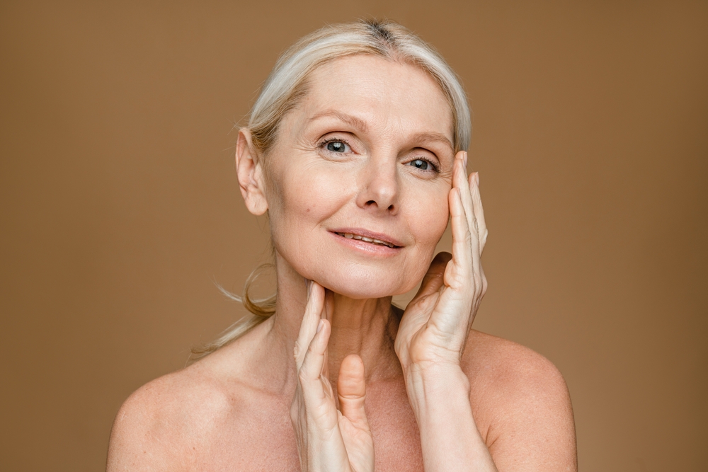 A well-aged woman caressing her face with her hands.