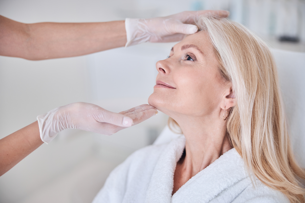 A woman looking up with gloved hands holding her face, analysing it for facial aesthetics in Arana Hills.