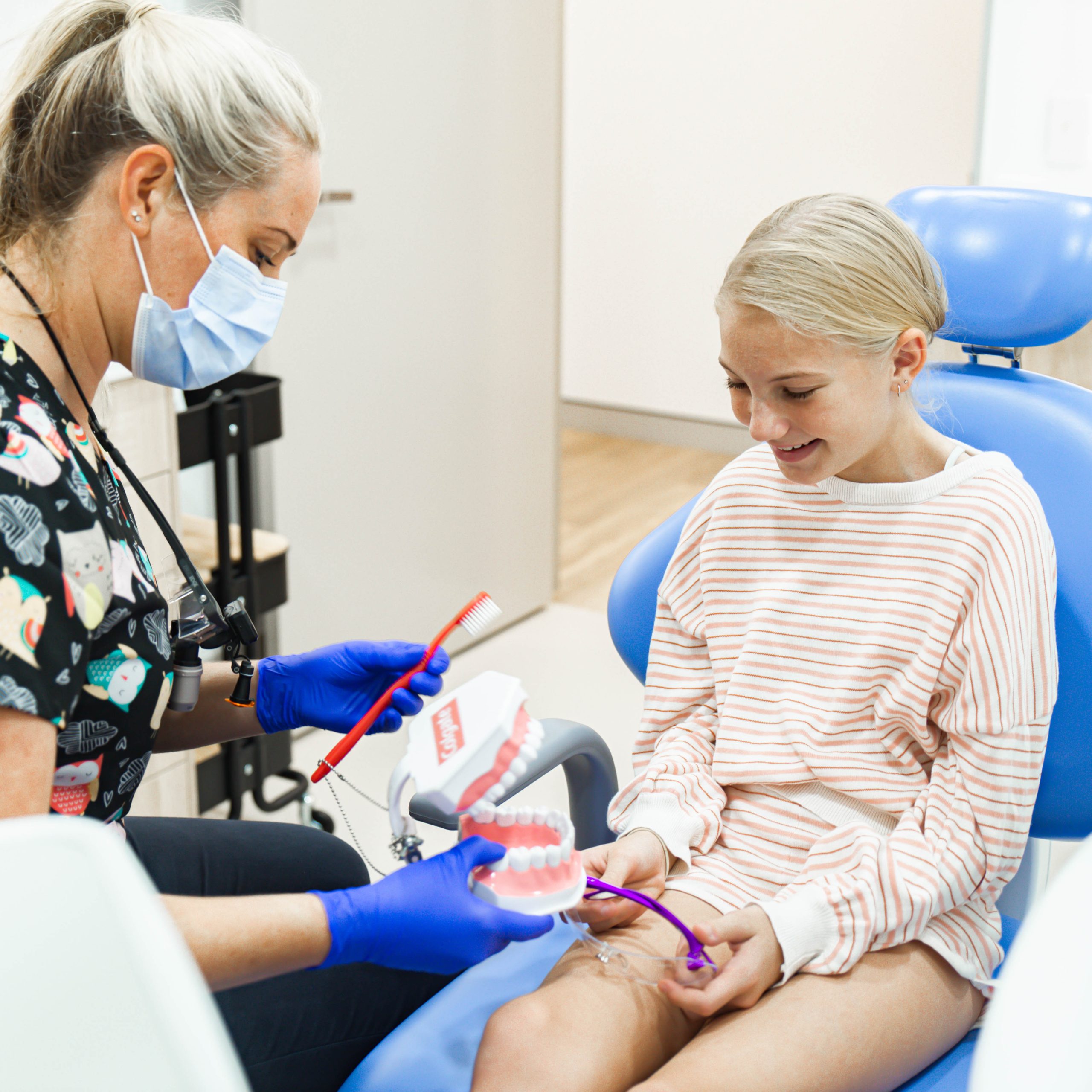 A dental professional at Admire Dentistry showing a young patient how to brush using a large anatomical model of teeth and a red toothbrush.