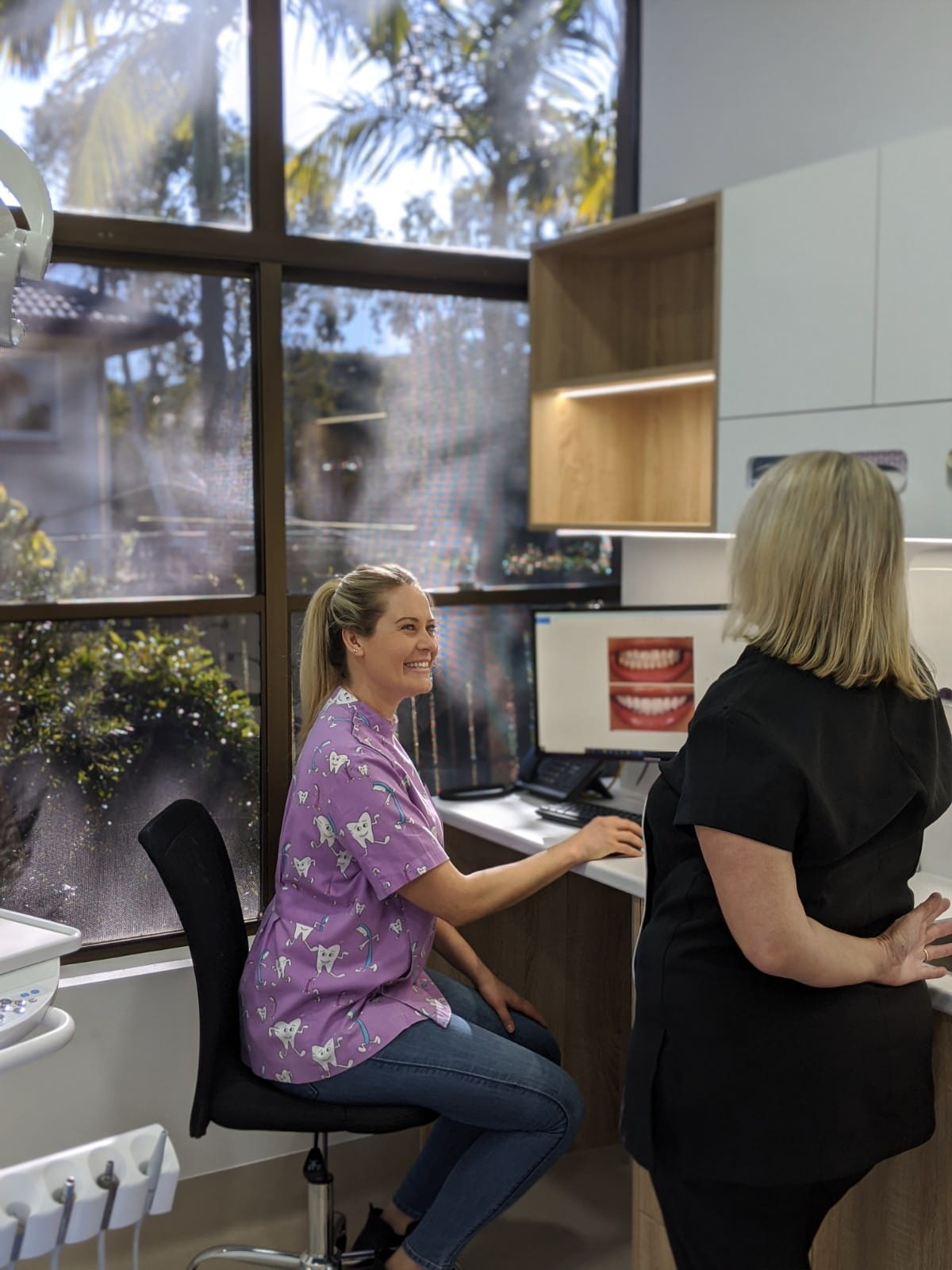 A smiling dental practitioner at Admire Dentistry reviewing a patient's treatment plan on a computer screen. 