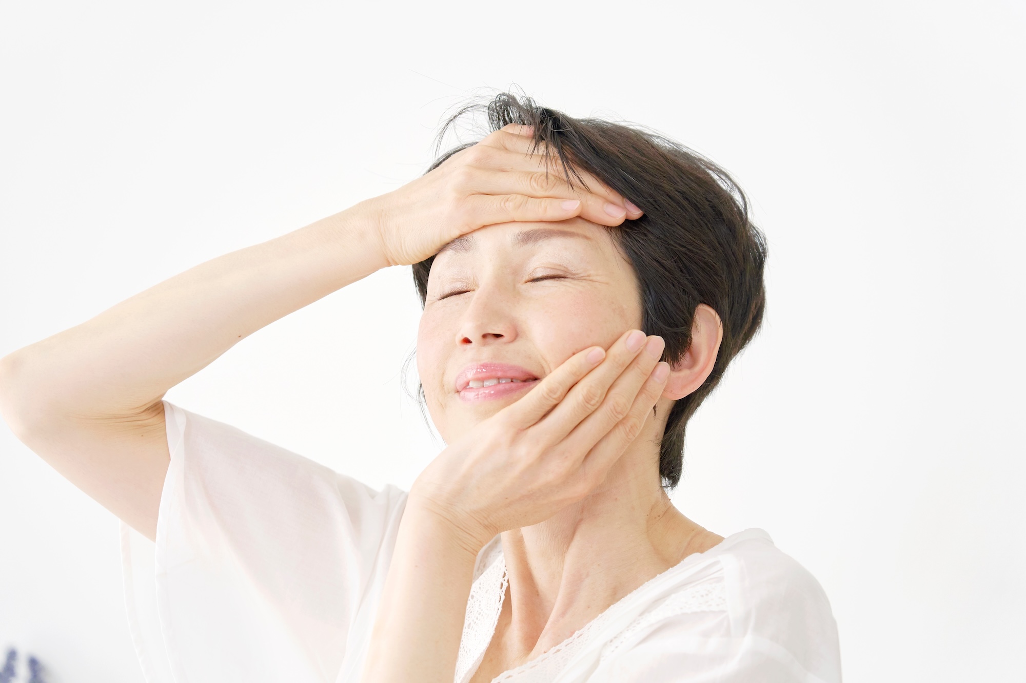 A mature woman smiling gently while touching her face to appreciate the results of her healthy menopausal skin care routine.