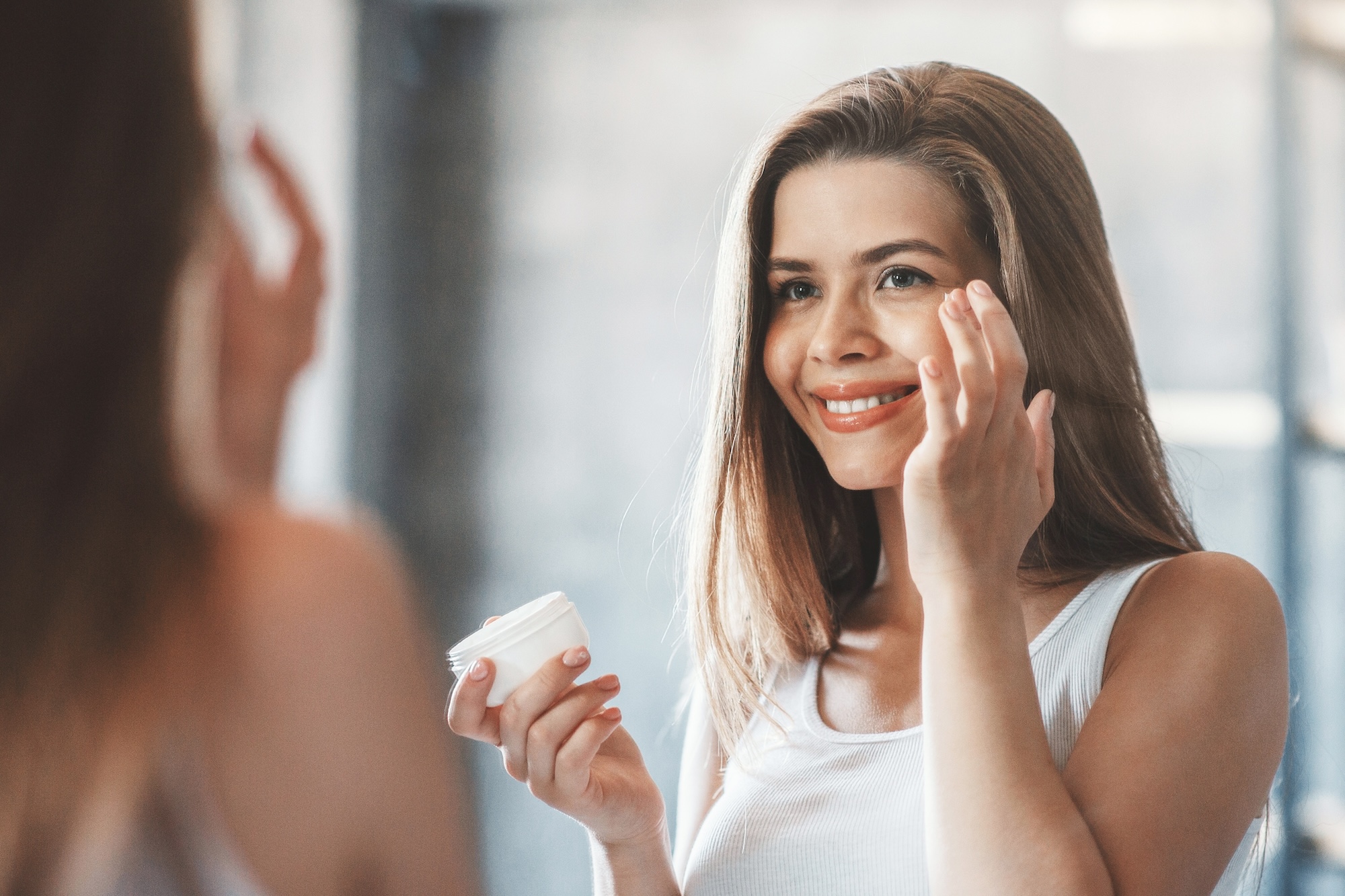 A woman applies a hydrating face cream in the mirror to protect her skin barrier against menopausal skin changes.