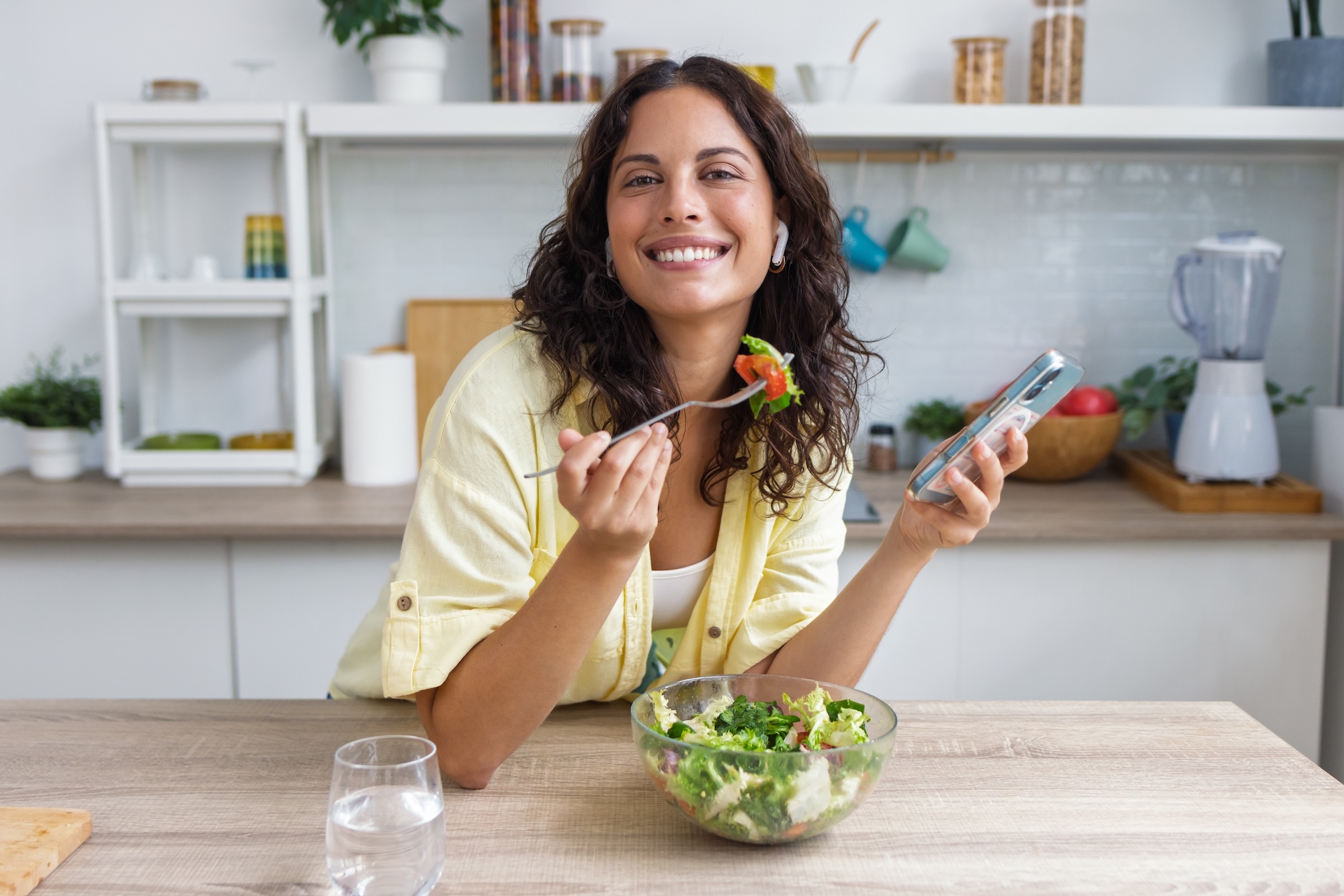 A smiling woman enjoys a fresh green salad in her kitchen to nourish her skin and body from within during menopause. 