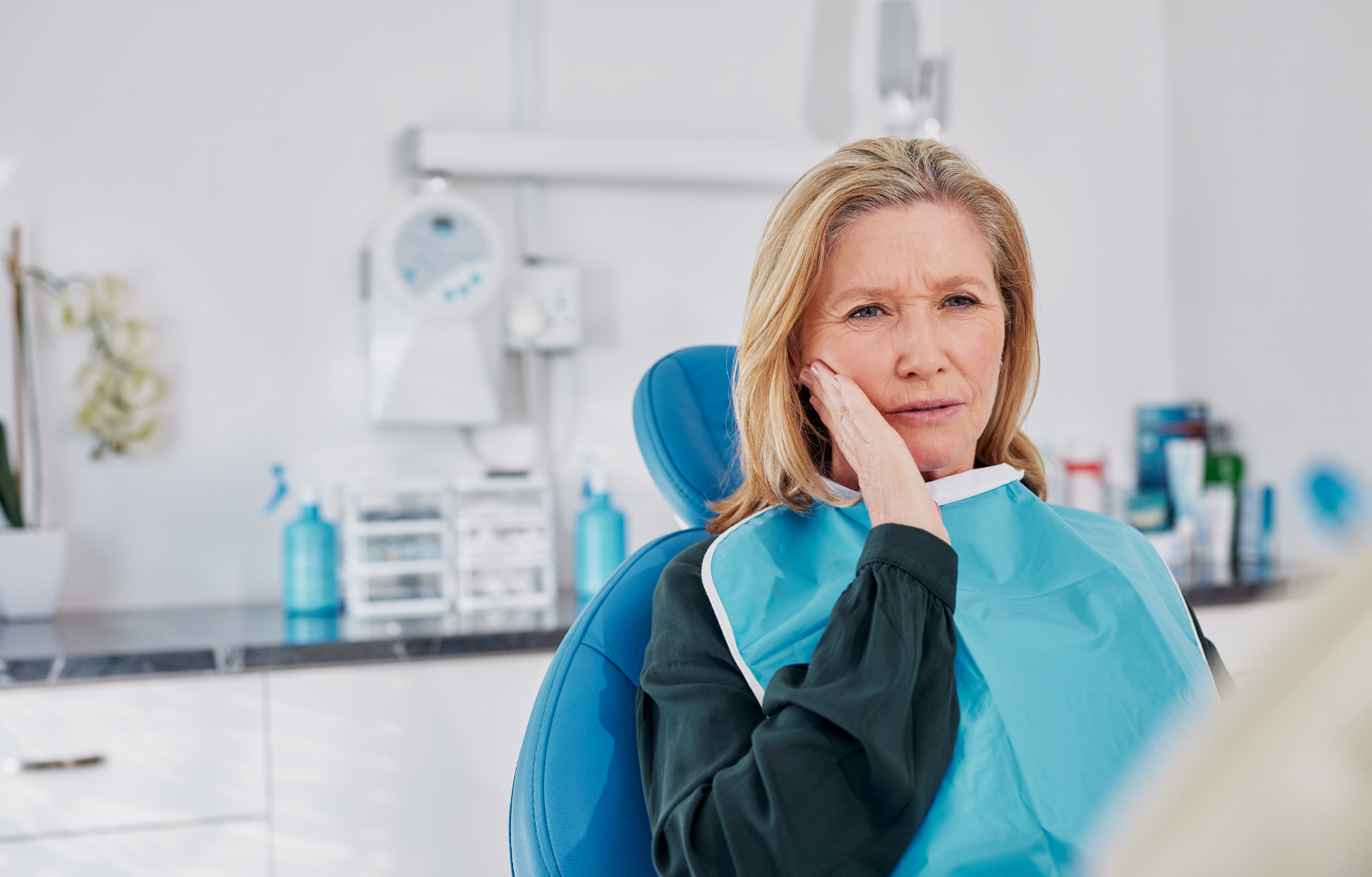 Woman holding her cheek in pain while sitting in a dental chair. 